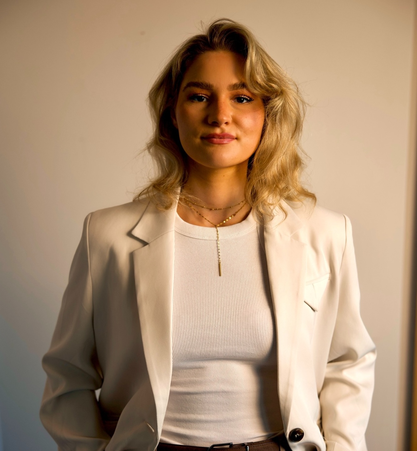 Blonde Frau mit hellem Blazer guckt in die Kamera