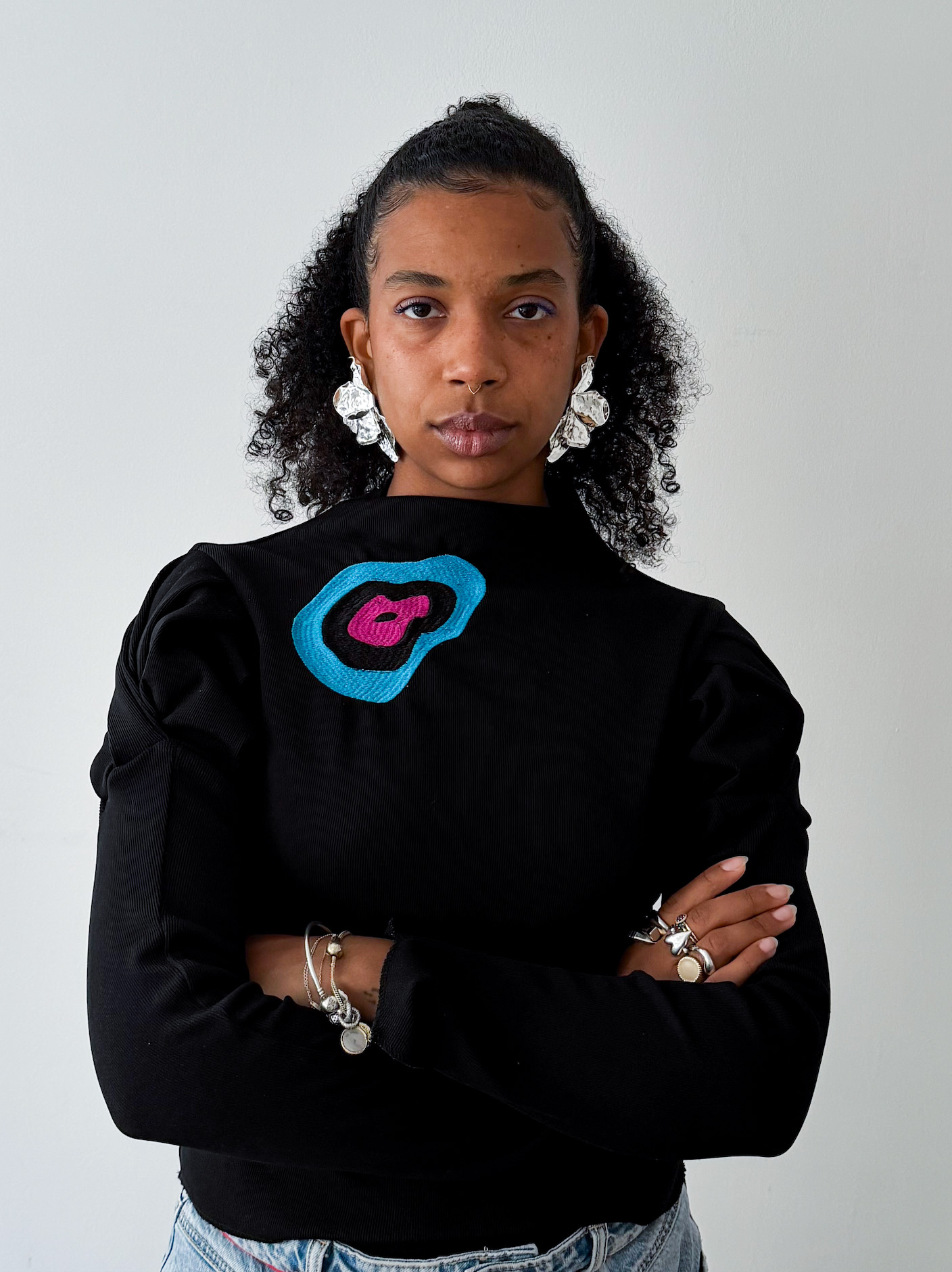 Portrait einer light-skinned mixed-race Frau mit Afrohaar, schwarzem Oberteil und direktem Blick in die Kamera.