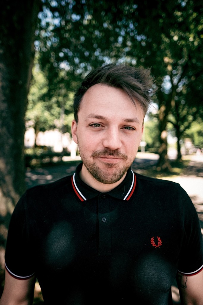 Ein Foto von Gavin Karlmeier. Einem Mann, der im schwarzen Poloshirt in einem Park steht. Sein Bild ist in die Kamera gerichtet.