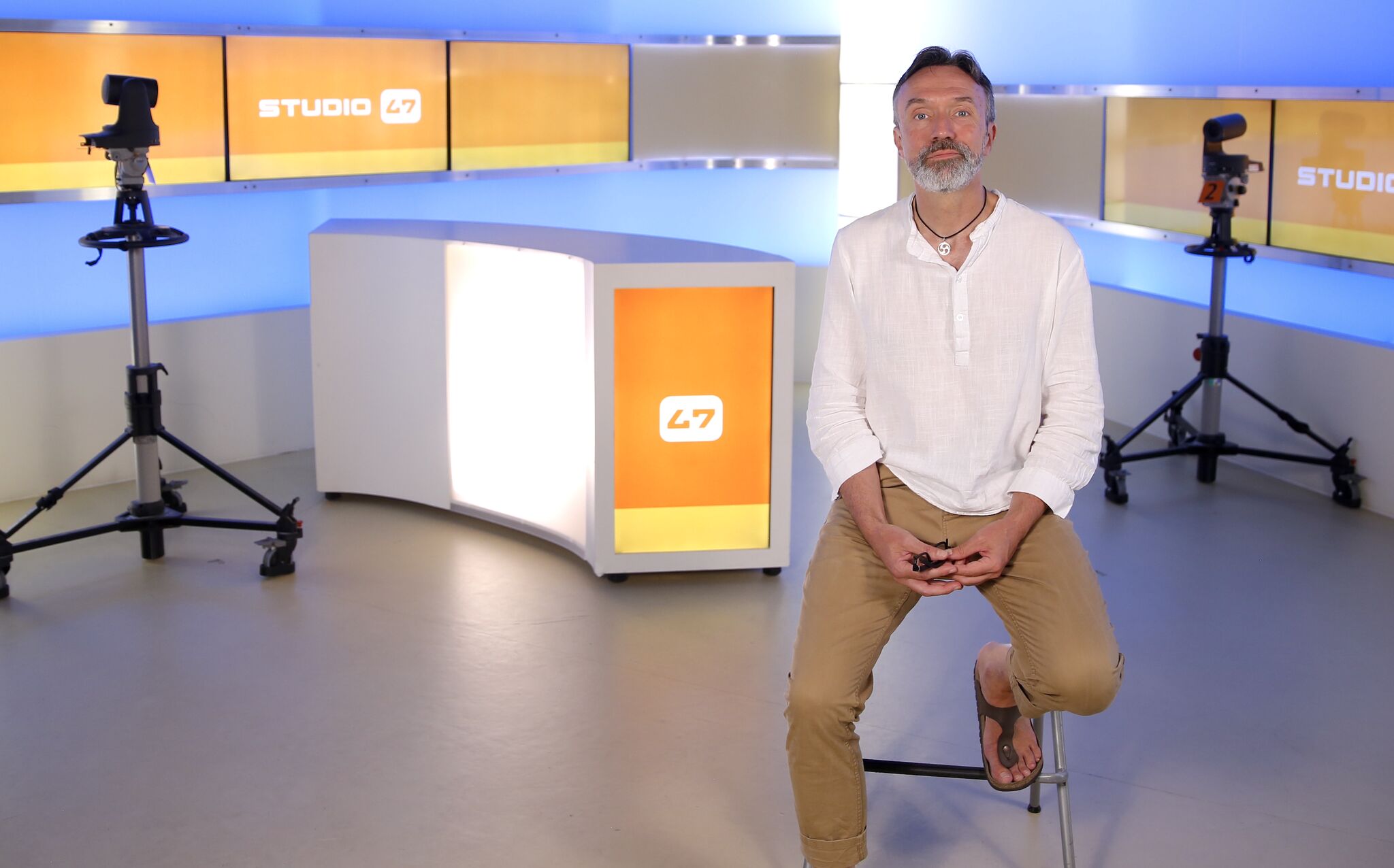 Sascha Devigne im TV-Studio von STUDIO 47, umgeben von Studiokameras, Moderationstresen und Bildschirmen mit dem Senderlogo.